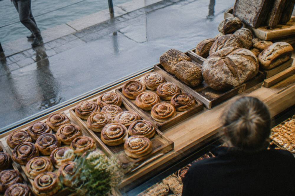 A bakery counter with cinnamon buns and breads stacked on wooden trays