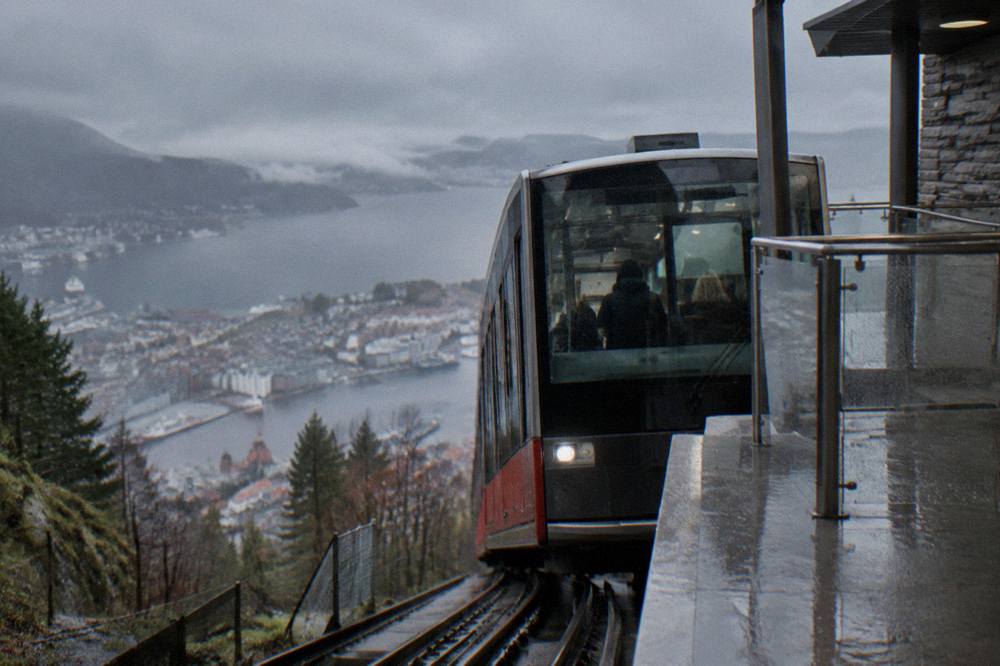 A funicular car arriving at an upper station with the city and fjord visible below