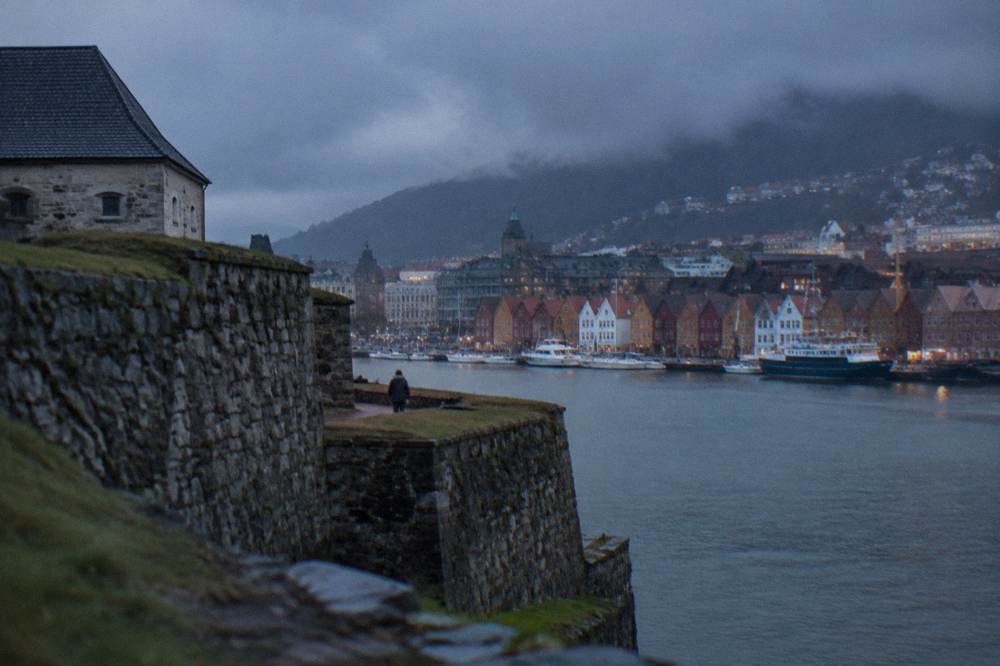 Stone walls of Bergenhus fortress beside the water with harbour buildings behind