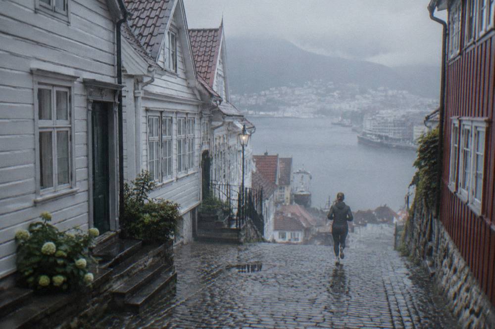 Old wooden buildings on a narrow uphill street in Bergen with wet cobbles