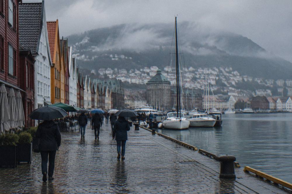 Visitors with umbrellas walking on wet cobblestones near the old wharf in Bergen