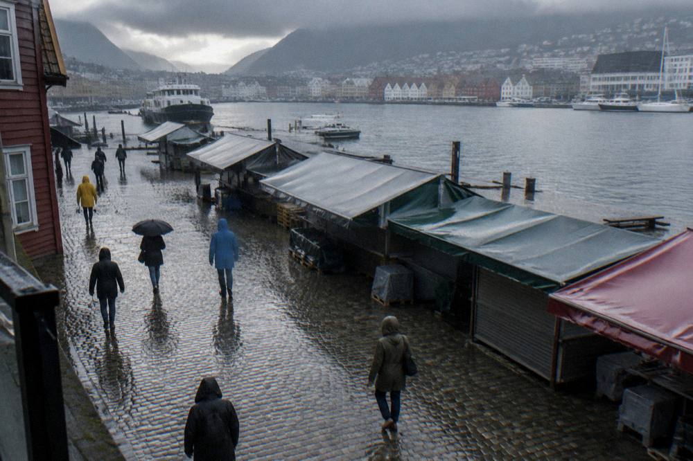 Rain-slicked cobbled street with people in raincoats walking past closed market stalls in early evening light