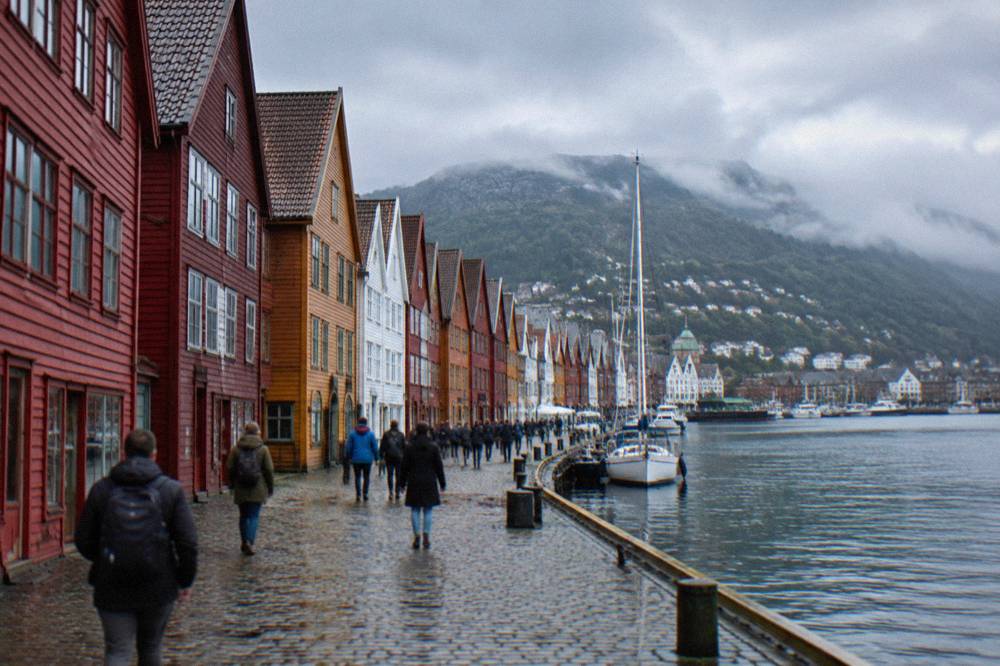Tourists walking between the colourful wooden Hanseatic buildings of the Bryggen wharf in Bergen on a bright day