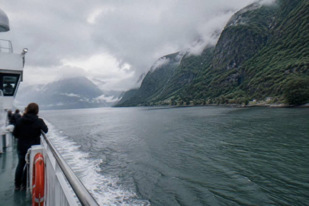 A passenger ferry crossing a narrow fjord with steep green cliffs and low clouds in western Norway