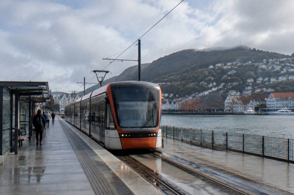 A modern light rail tram arriving at an outdoor station in Bergen with hills behind the houses