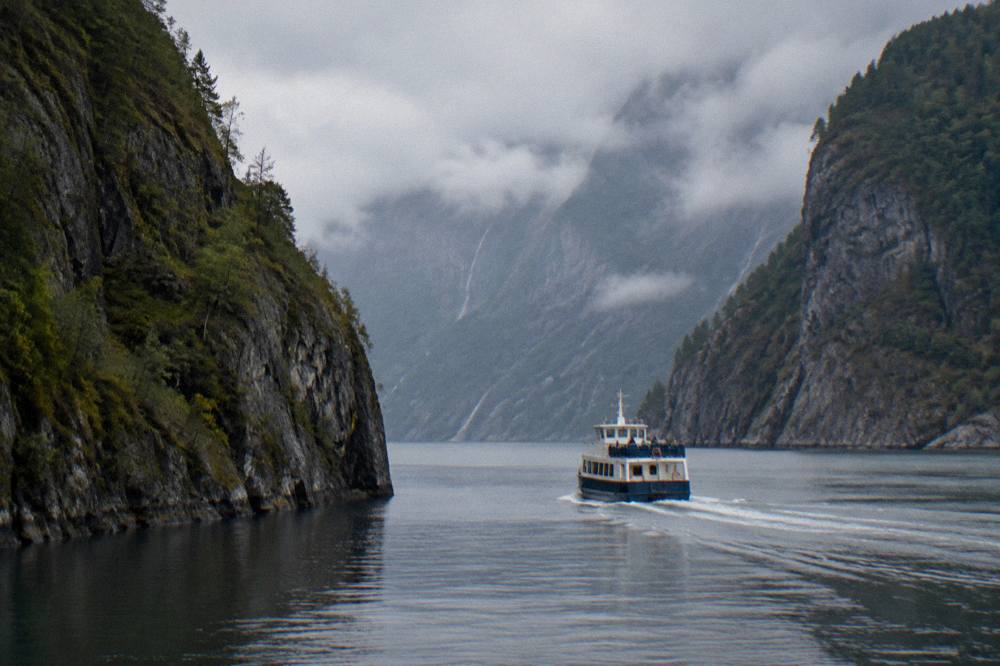 A small passenger boat cruising through a narrow fjord channel with steep rock walls rising on both sides