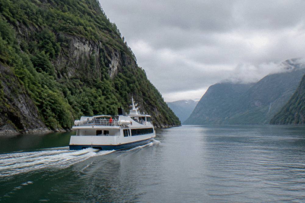 A fjord cruise boat cutting through calm water between steep green cliffs on the Osterfjord near Bergen