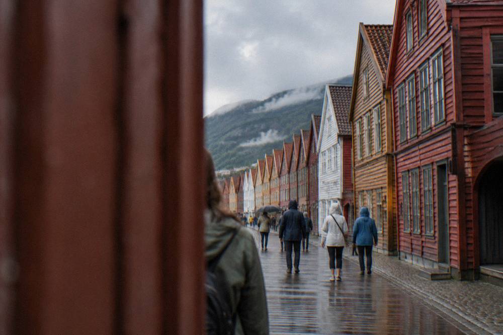 Visitors in light rain jackets walking the wooden walkways of Bryggen in Bergen on a mild summer afternoon