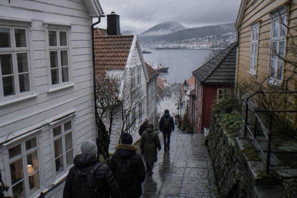 Travellers in winter coats following a guide along a narrow lane between old wooden buildings in Bergen