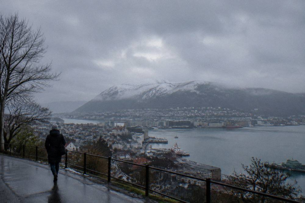 A snow-covered mountain ridge rising above a grey rain-streaked Bergen city and its harbour waters