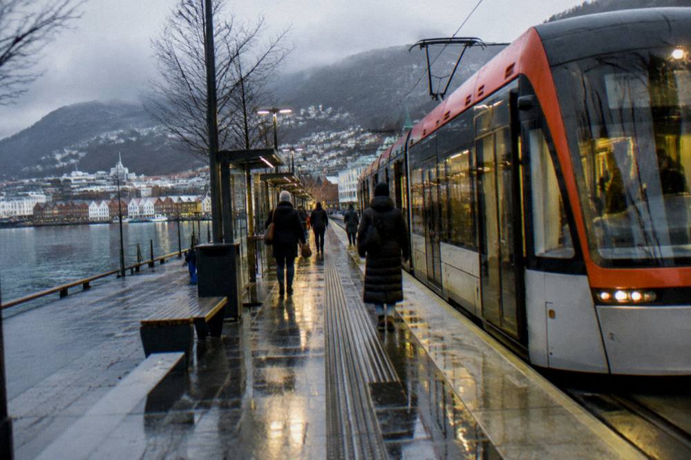 A modern light rail tram stopped at an illuminated city-centre platform on a wet winter evening