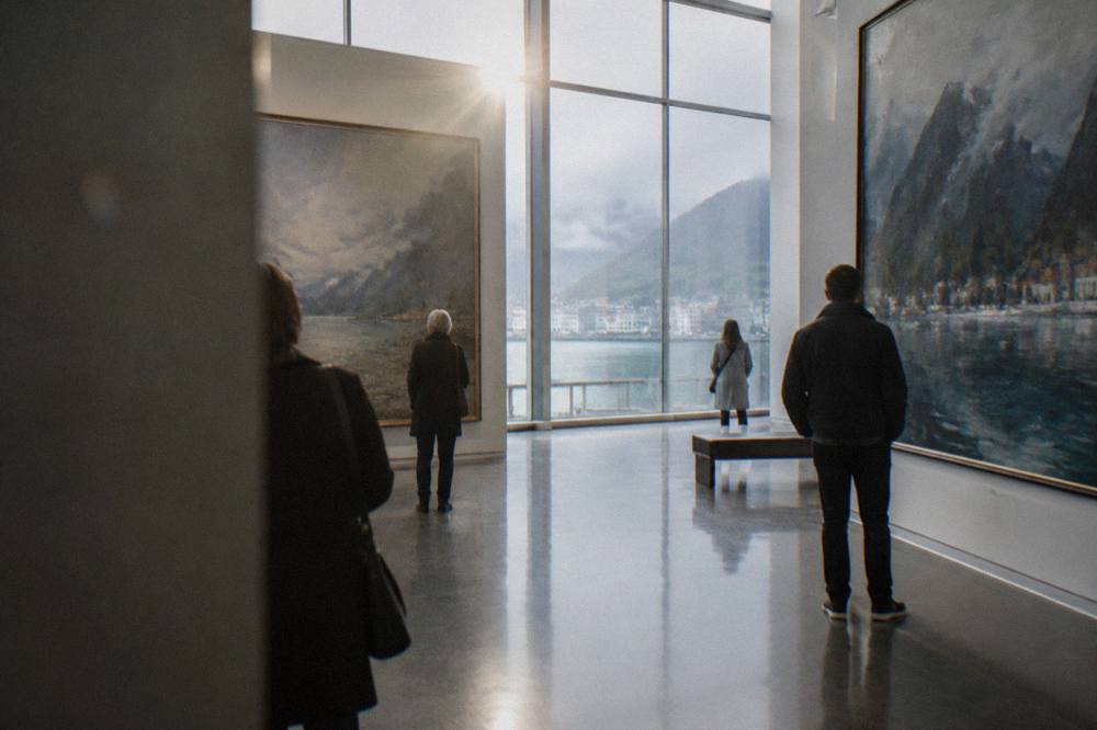 Gallery visitors viewing large oil paintings in a bright Bergen art museum hall