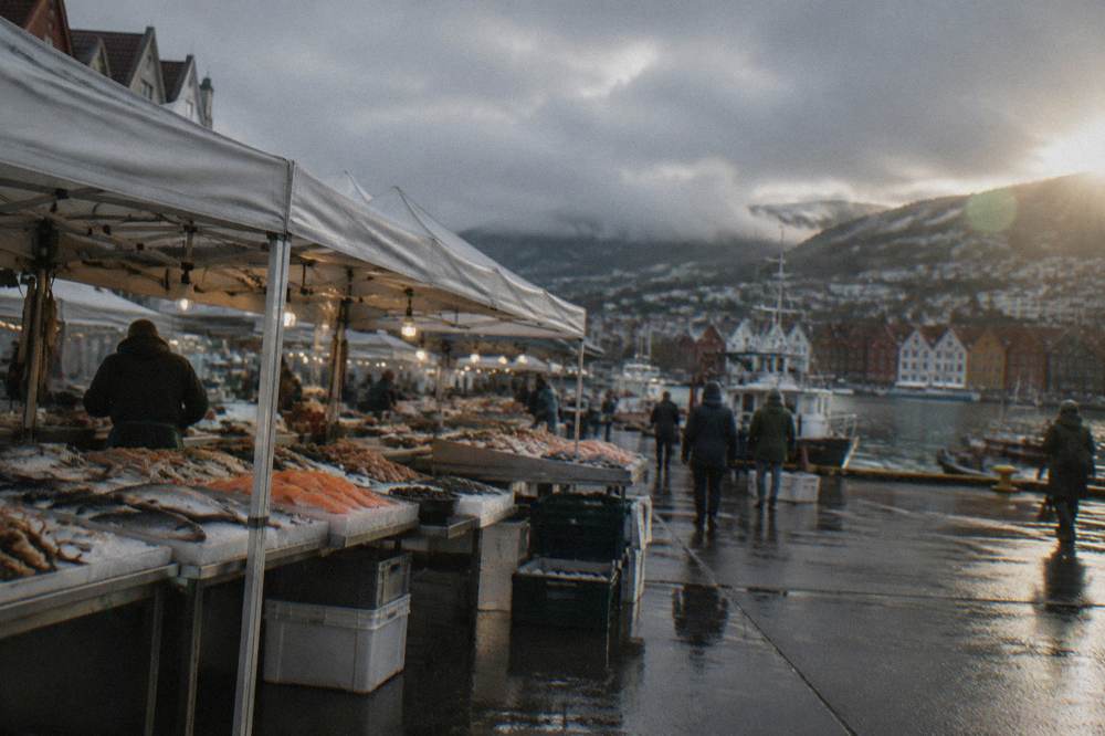 Outdoor food stalls under white canopies at a Norwegian fish market in the evening