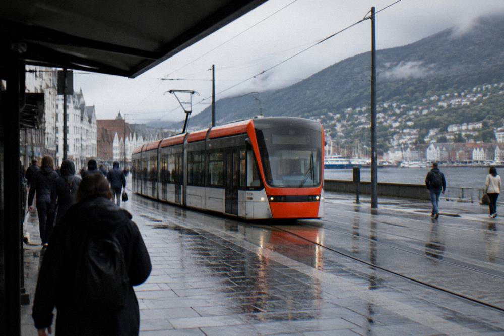 Modern light rail tram travelling along a street in central Bergen past pedestrians