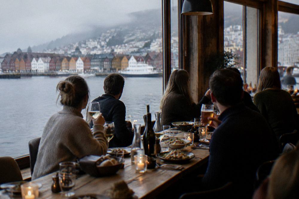 Friends sharing food and drinks at a long wooden table in a warm restaurant