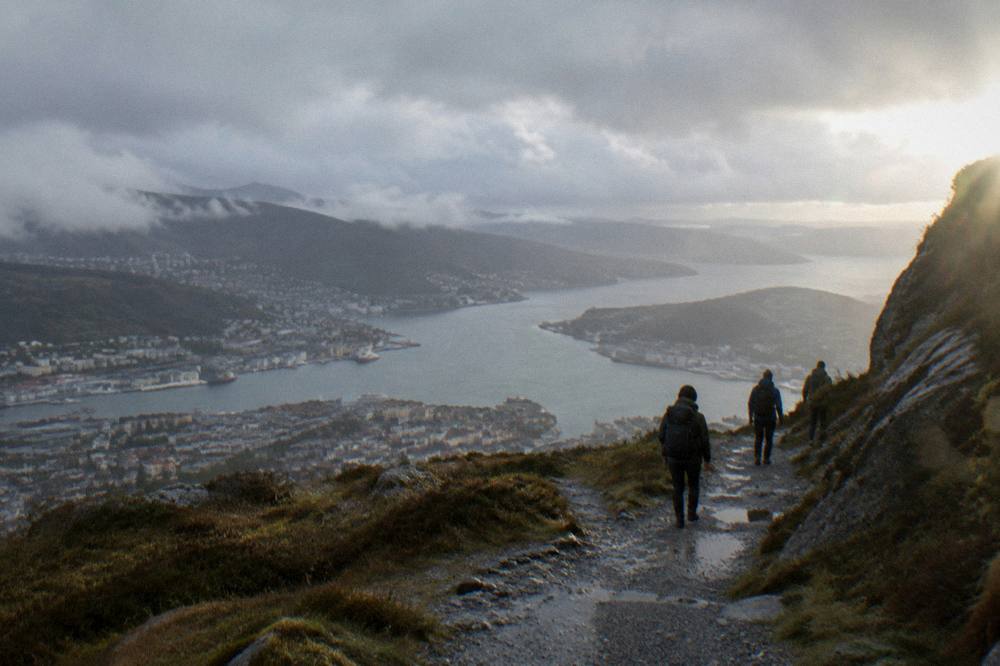 Hikers on a gravel trail above the tree line overlooking Bergen and its fjord