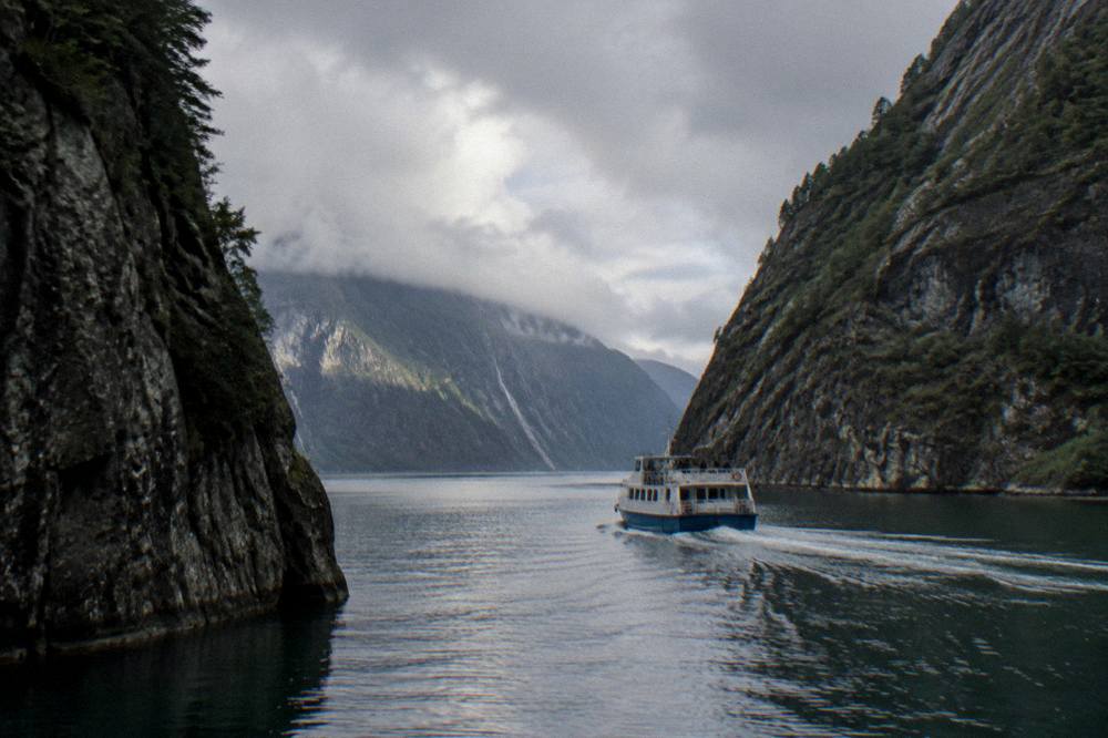 A small passenger boat cruising between steep rocky cliffs on a narrow Norwegian fjord