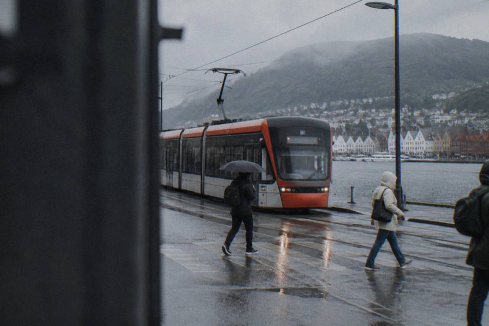 A light rail tram travelling along a street in Bergen with pedestrians crossing nearby