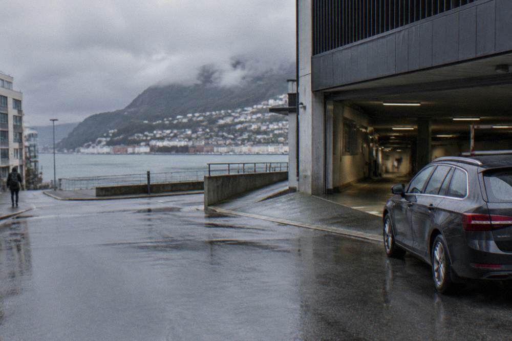 A parked car beside a modern parking garage entrance in a Norwegian city street
