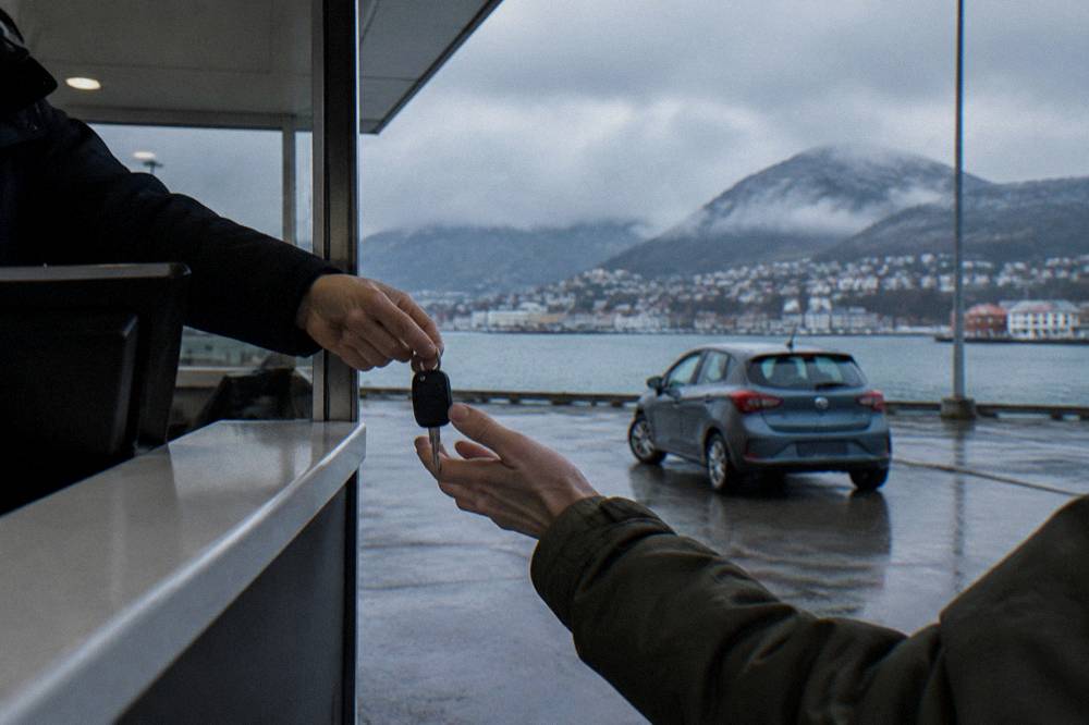 A rental car key handover at an airport counter with a compact car parked outside