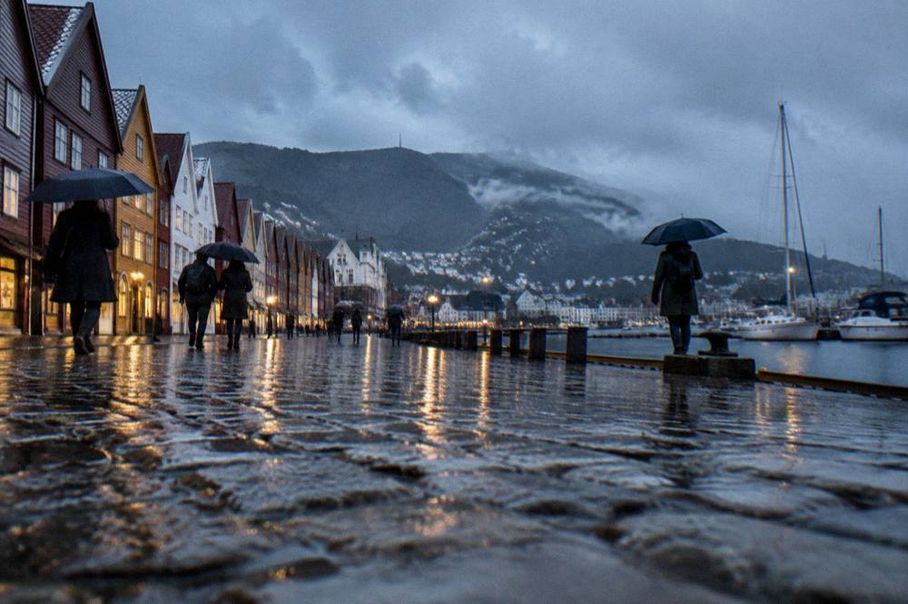 Rainy street in Bergen with wet reflective cobblestones and people under umbrellas