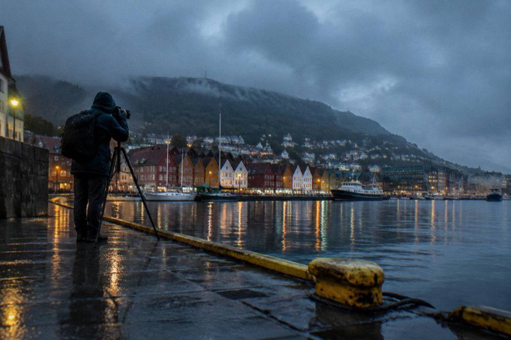 Photographer with a tripod photographing harbor lights during deep blue twilight