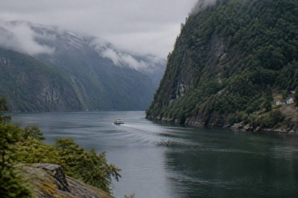 Steep forested cliffs dropping into a narrow fjord channel with a small boat wake