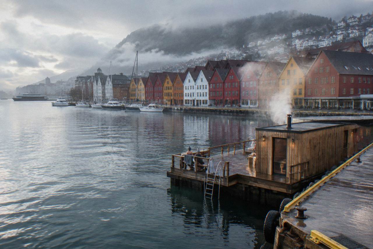 Steam rising from a wooden sauna on a Bergen harbour pier with colourful buildings behind it