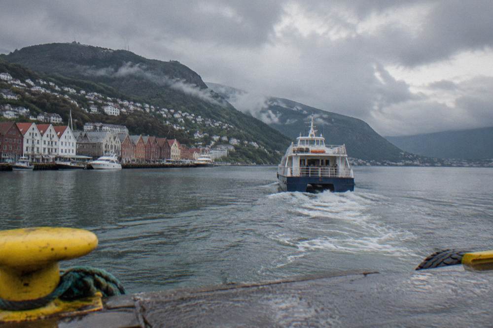 A fjord boat departing from Bergen harbour with mountains rising behind the water
