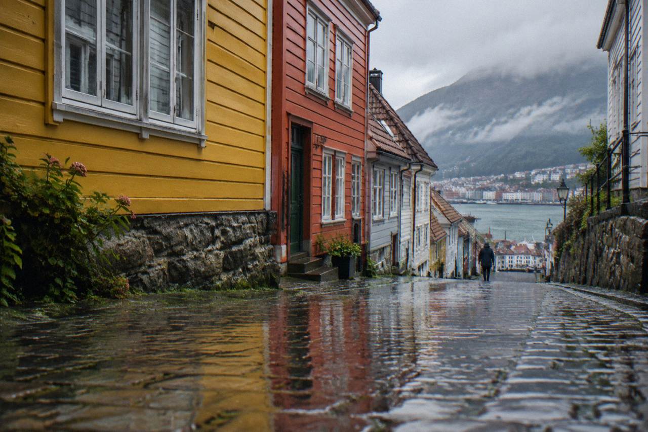 A colourful painted wall on a narrow street of wooden townhouses in Bergen, Norway, with wet cobblestones reflecting the colours.
