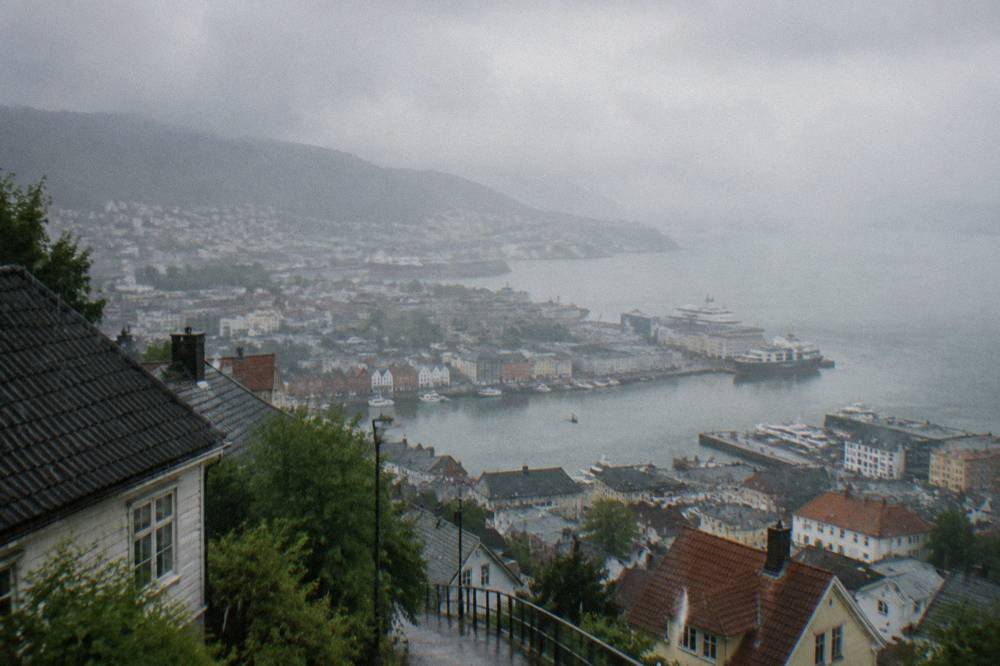 Rain streaks running down a faded mural on a Bergen wall under a grey sky.