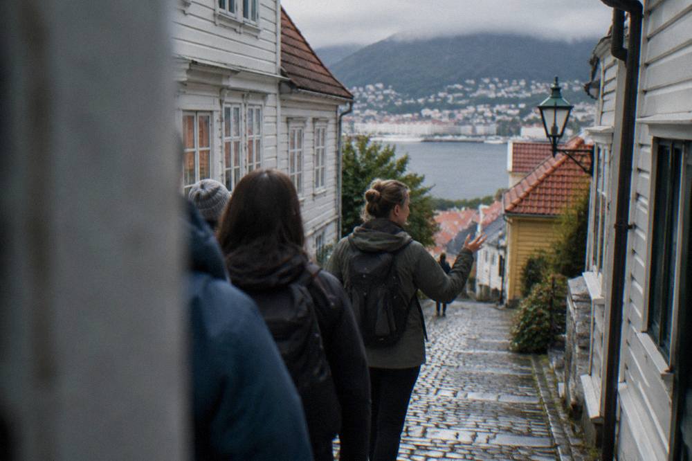 A local guide leading a small group of visitors through a narrow cobbled lane in central Bergen
