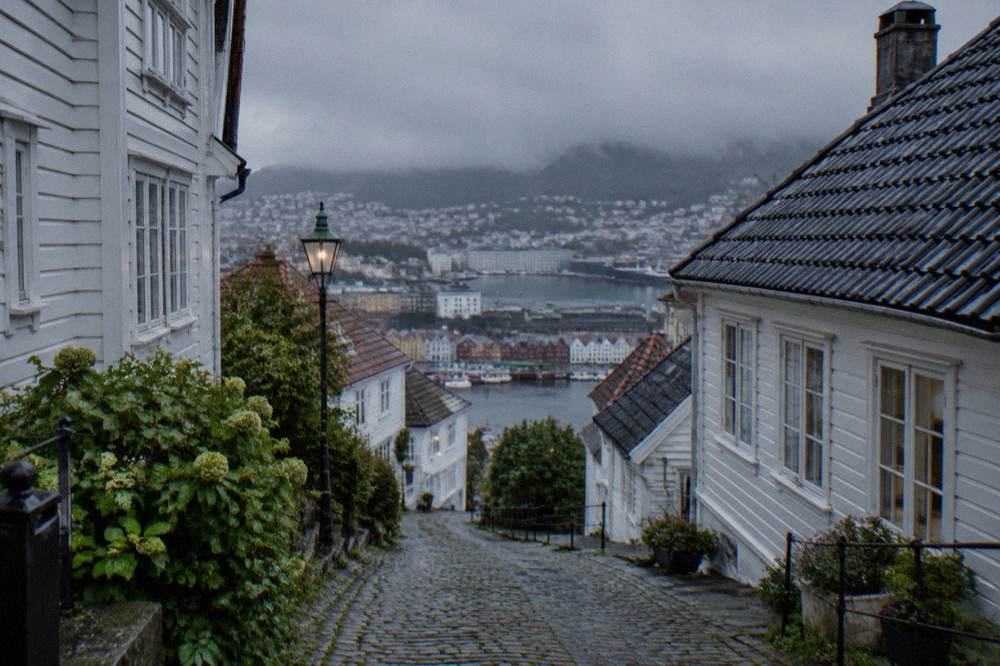 A steep narrow cobbled lane with white wooden houses climbing the hillside above central Bergen