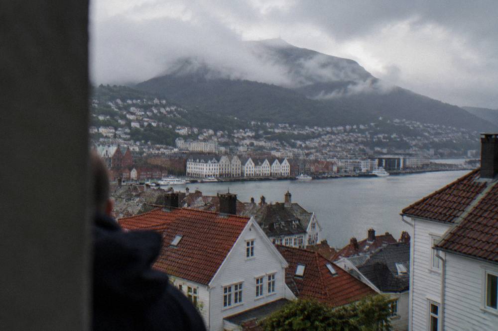 View over red and white Bergen rooftops toward a mountain summit partly hidden by low cloud