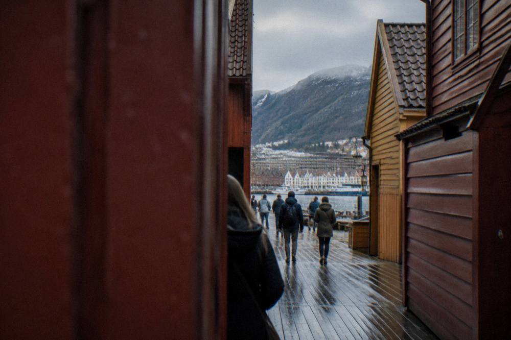 Visitors walking through the narrow wooden buildings of the old wharf in Bergen on a bright clear evening