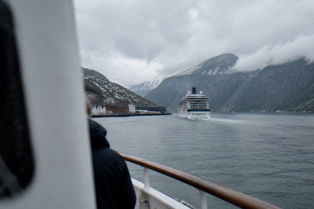 A cruise boat heading out from a Norwegian harbour toward steep fjord mountains