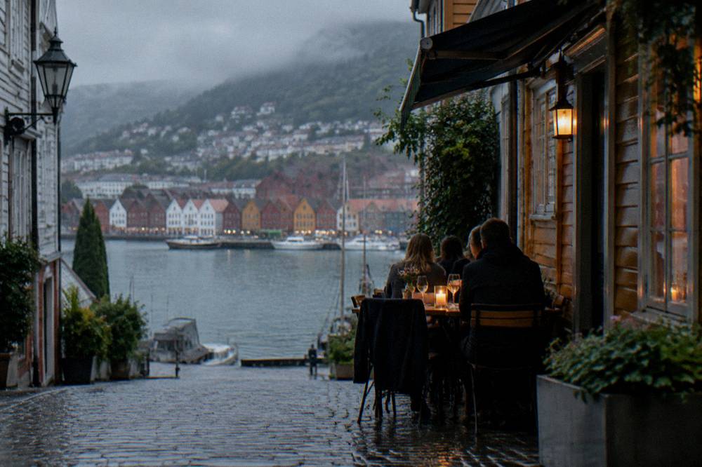 Diners at a small candle-lit restaurant table in a narrow Bergen side street