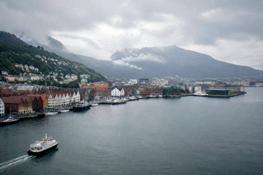 The Bergen city skyline with mountains behind it under a partly cloudy sky seen from the water