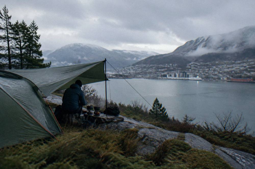A camper cooking dinner under a tarp beside a small tent in soft evening light
