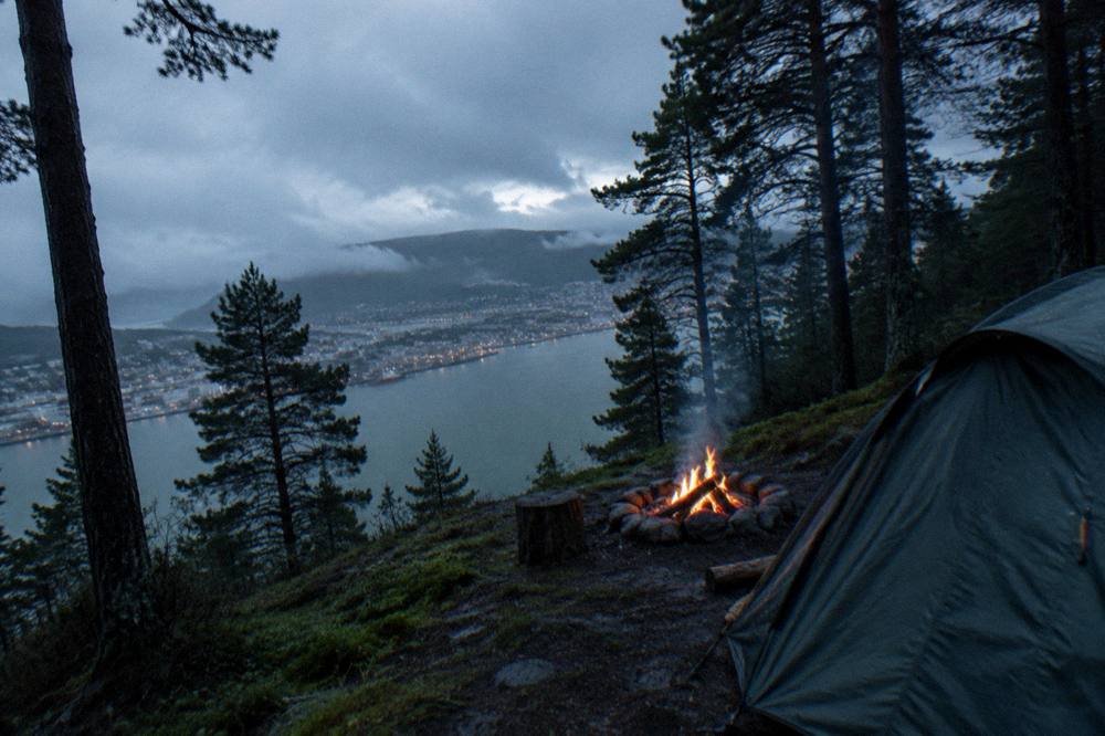 A small campfire burning beside a tent at dusk with dark pine forest around