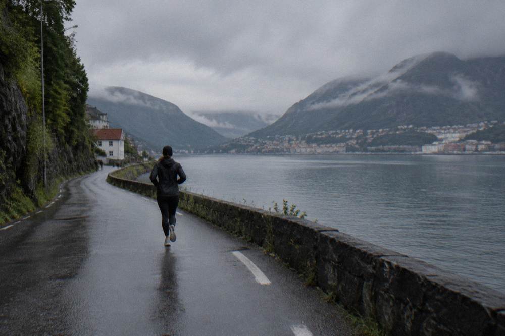 A narrow road winding along the shore of a fjord with steep mountains rising above the water