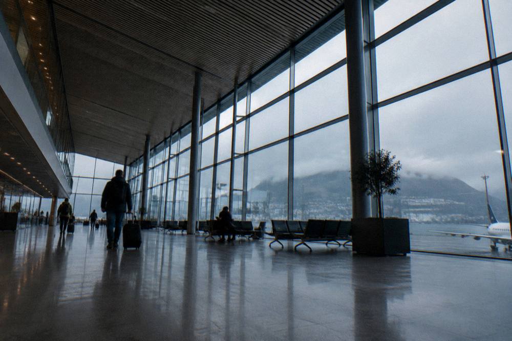 A modern airport terminal hall with departure boards and travellers with luggage
