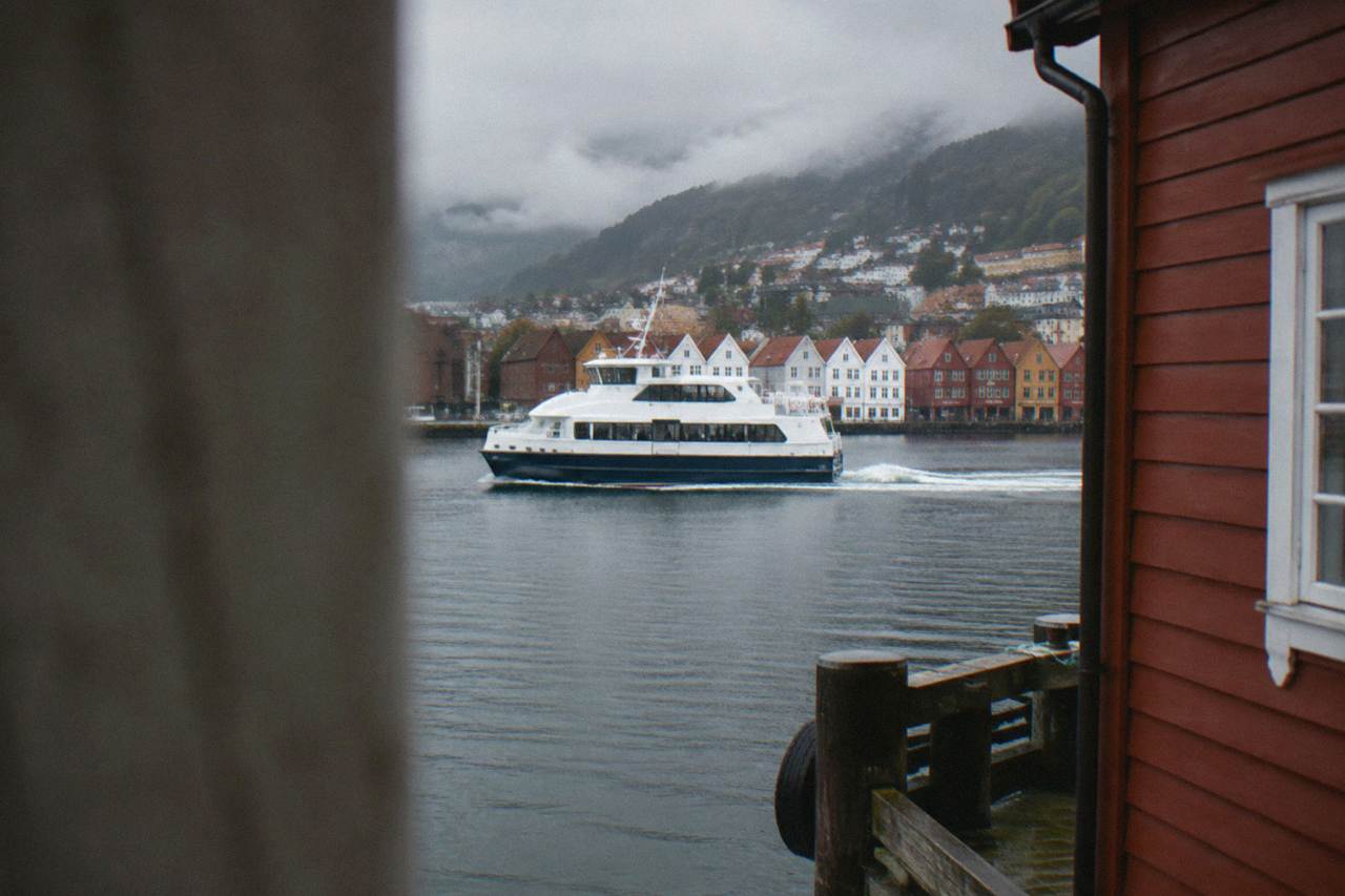 A passenger ferry moving across calm water between wooden buildings on the Bergen waterfront