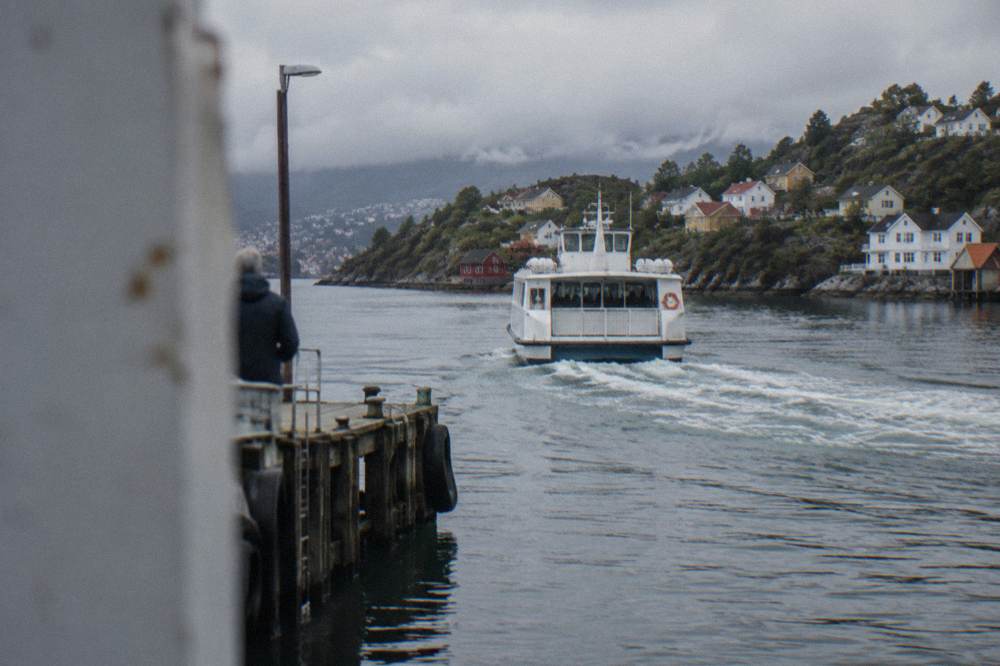 A small white commuter ferry pulling away from a wooden jetty with island houses behind it