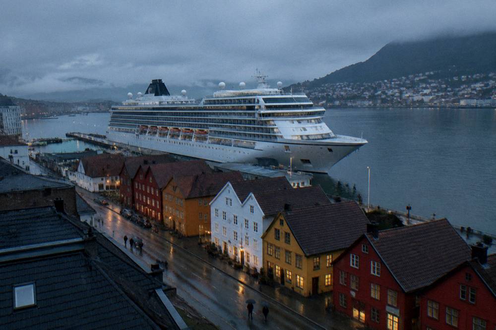 A large cruise ship docked at a quay with a row of coloured wooden buildings in the foreground