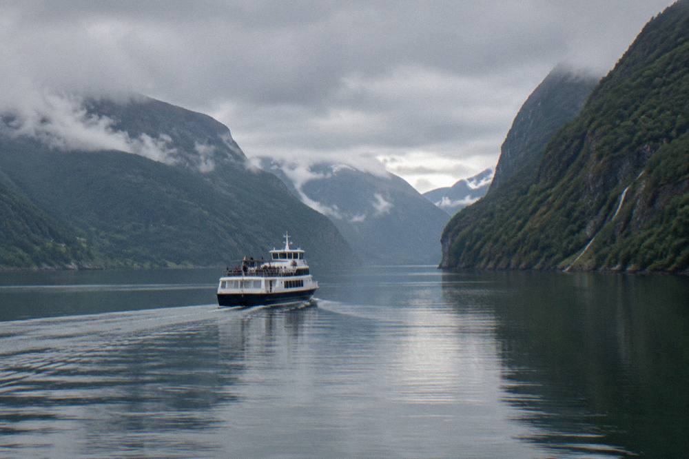 A tour boat travelling on a mirror calm fjord with steep green mountainsides rising on both sides