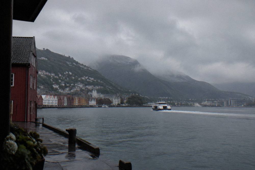 Rain clouds passing over a fjord with a tour boat leaving a light trail on the dark water