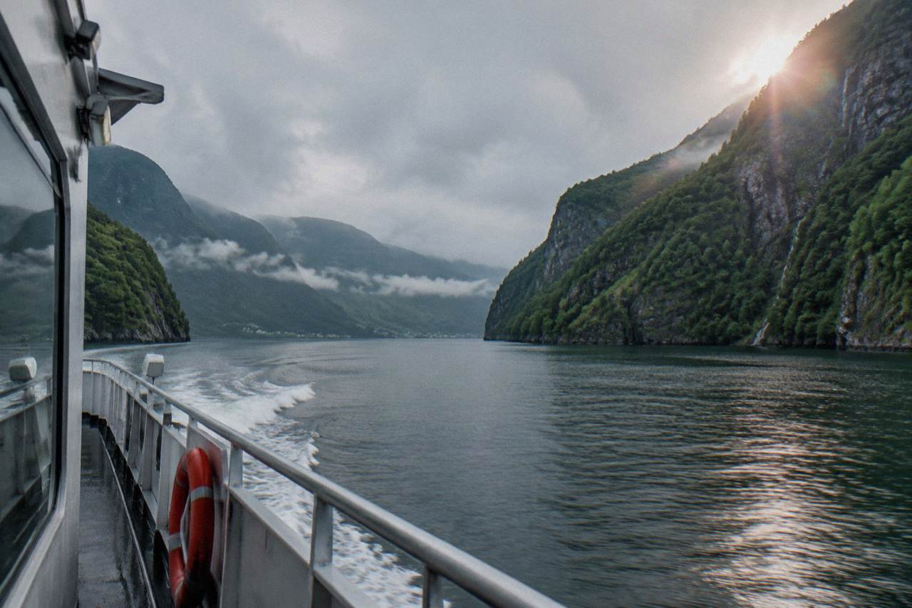 A passenger boat sailing a narrow fjord between steep green cliffs in western Norway