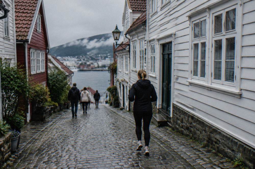 Tourists walking along a narrow cobbled street between old wooden houses in Bergen