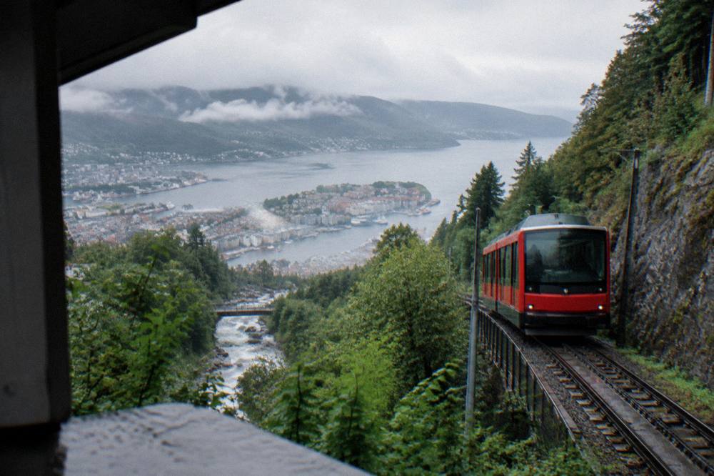 A red train climbing a steep mountain railway beside a river in western Norway
